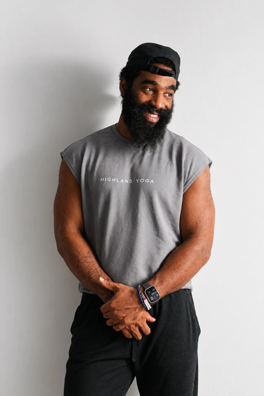 A smiling person wearing a charcoal Highland Yoga sleeveless tee and black cap